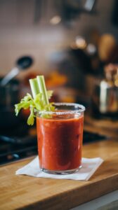 Bloody Mary cocktail with celery stick garnish in a glass with a salt rim on a wooden counter.